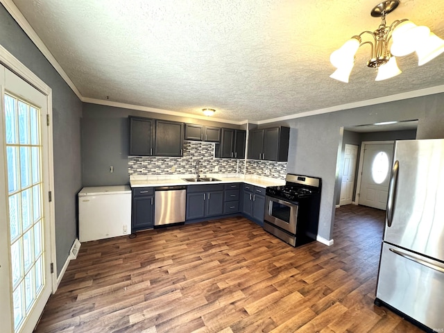 kitchen featuring a chandelier, appliances with stainless steel finishes, wood finished floors, light countertops, and a sink