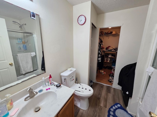 full bath with wood finished floors, a shower stall, toilet, vanity, and a walk in closet