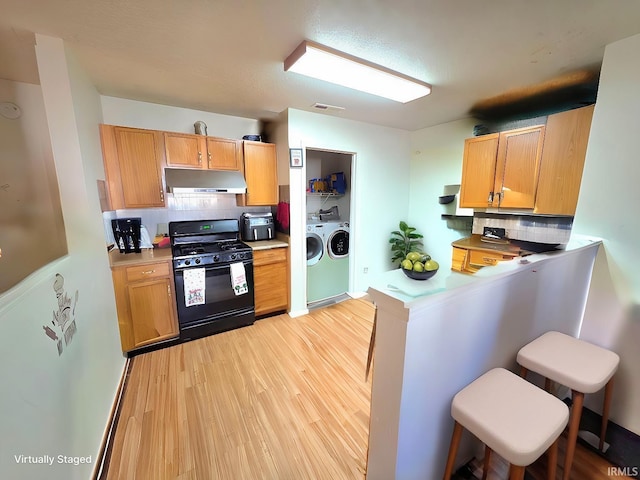 kitchen featuring separate washer and dryer, decorative backsplash, under cabinet range hood, light wood finished floors, and black range with gas cooktop