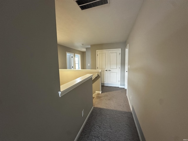 corridor featuring dark carpet, visible vents, and baseboards