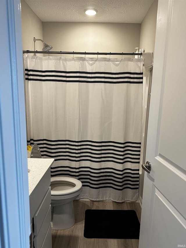 bathroom with a textured ceiling, vanity, toilet, curtained shower, and wood finished floors