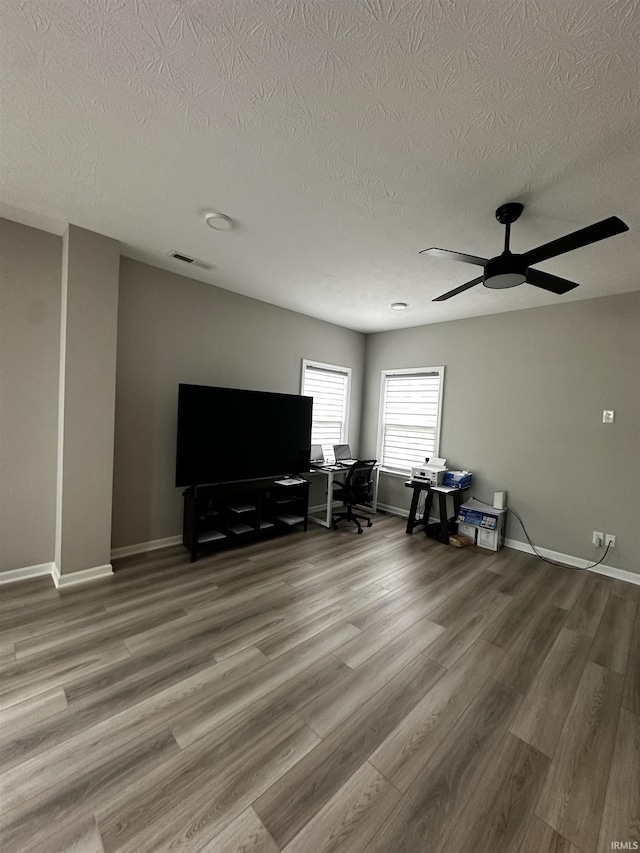 unfurnished living room featuring visible vents, baseboards, a ceiling fan, and wood finished floors