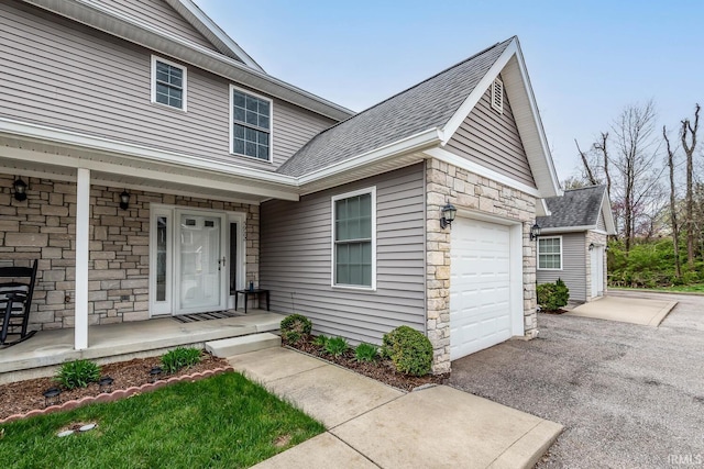 5922 N Ajuga Ct, Ellettsville, IN 47429 - view of exterior entry featuring driveway, stone siding, roof with shingles, covered porch, and a garage