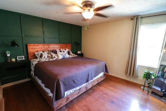 bedroom featuring baseboards, a textured ceiling, a ceiling fan, a decorative wall, and wood finished floors