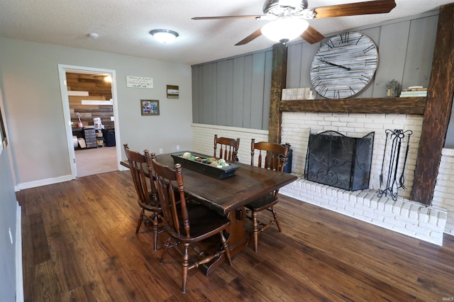 dining area with a brick fireplace, a textured ceiling, a ceiling fan, and wood finished floors