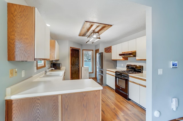 kitchen featuring light countertops, white cabinets, under cabinet range hood, black gas range, and a sink