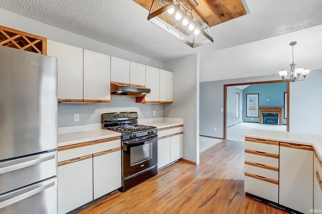 kitchen with freestanding refrigerator, black range with gas stovetop, under cabinet range hood, light countertops, and a notable chandelier