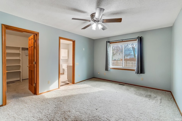 unfurnished bedroom with visible vents, baseboards, a textured ceiling, a walk in closet, and carpet flooring