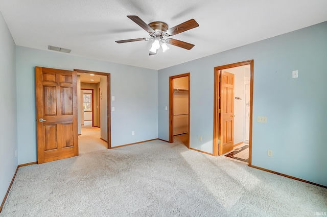 unfurnished bedroom featuring a walk in closet, light colored carpet, baseboards, and visible vents