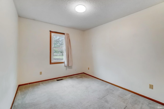 carpeted spare room featuring visible vents, a textured ceiling, and baseboards