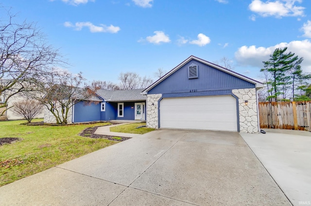 view of front of house with concrete driveway, stone siding, a front yard, a garage, and fence