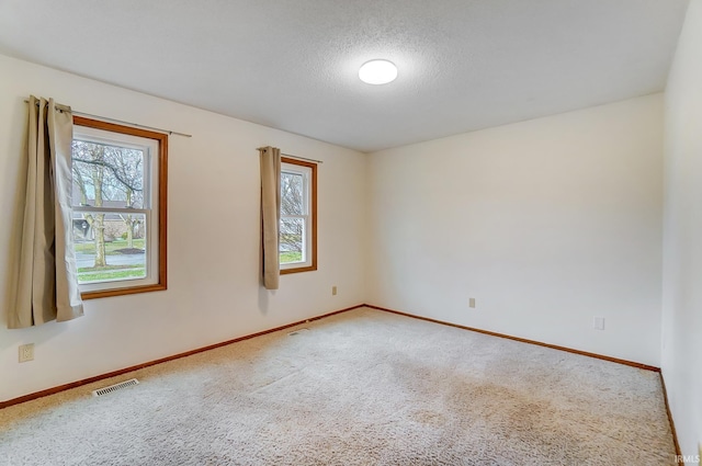 carpeted spare room featuring visible vents, baseboards, and a textured ceiling