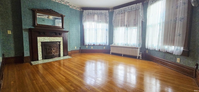 126 E 4th St, Mount Carmel, IL 62863 - unfurnished living room featuring radiator, wood finished floors, wallpapered walls, and a stone fireplace