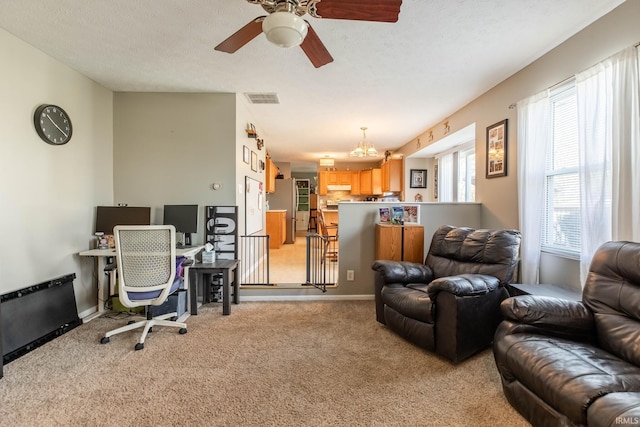 living area featuring visible vents, baseboards, a textured ceiling, ceiling fan with notable chandelier, and light carpet