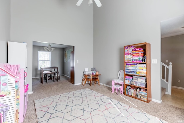 playroom with baseboards, carpet flooring, a towering ceiling, and ceiling fan with notable chandelier