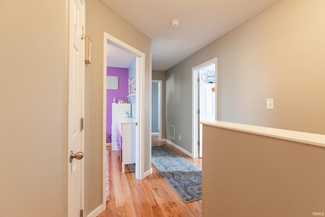 hall featuring visible vents, light wood-type flooring, and baseboards