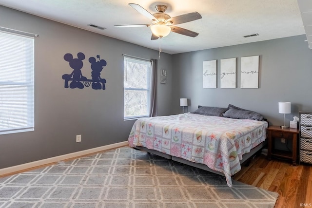 bedroom with ceiling fan, visible vents, baseboards, and wood finished floors