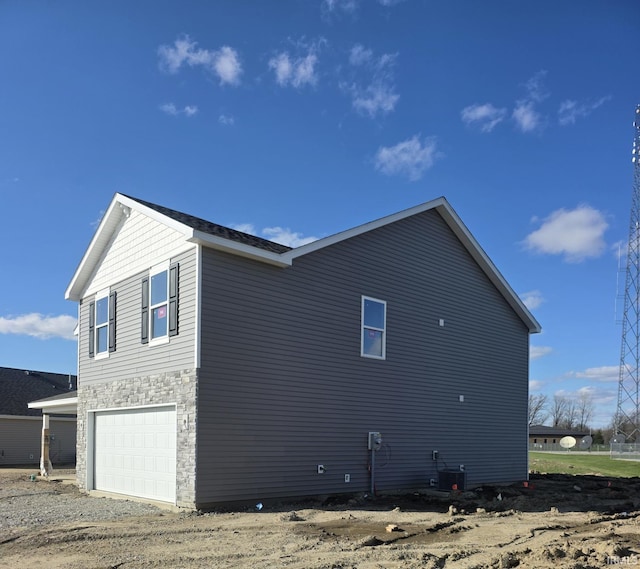 view of home's exterior featuring driveway, a garage, stone siding, and central AC