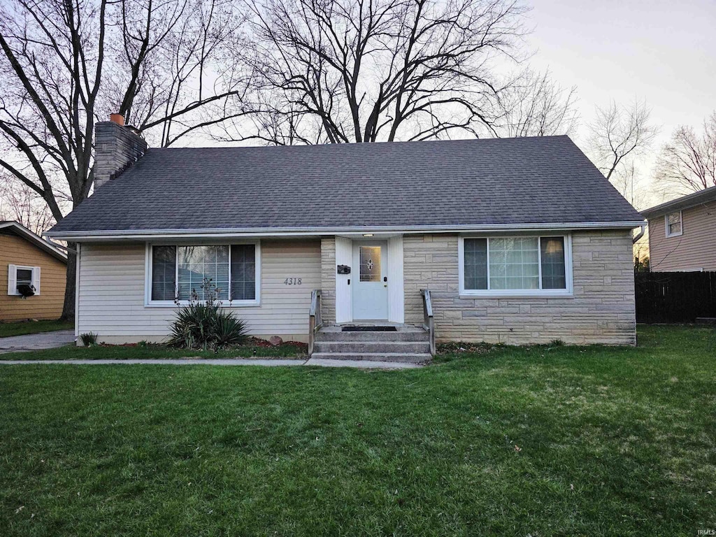 ranch-style house with a shingled roof, stone siding, a chimney, and a front lawn