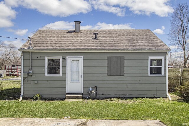 back of house featuring a yard, entry steps, a chimney, fence, and roof with shingles