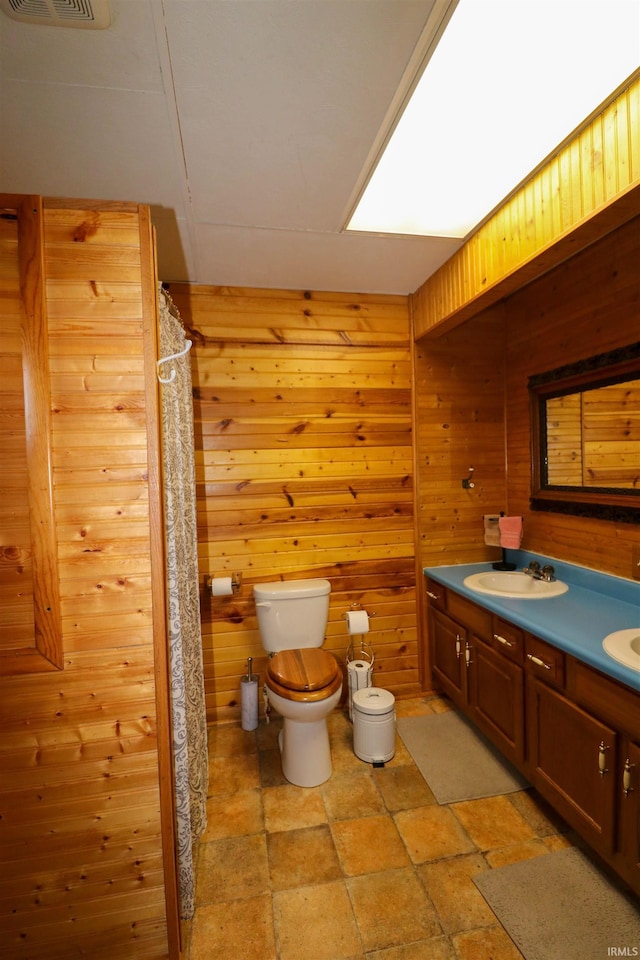 bathroom with double vanity, wooden walls, toilet, visible vents, and a sink