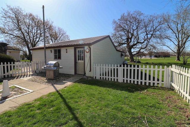 rear view of house with metal roof, fence private yard, an outdoor structure, and a lawn