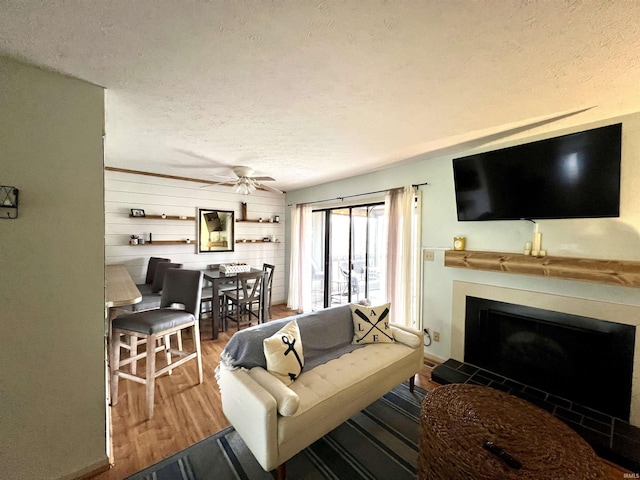 living room with a fireplace, a textured ceiling, a ceiling fan, and wood finished floors
