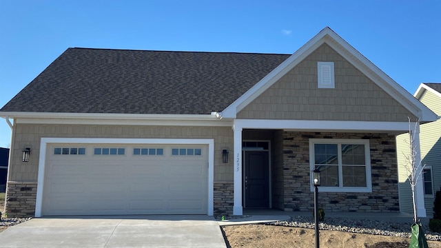 view of front of home featuring a garage, roof with shingles, driveway, and stone siding