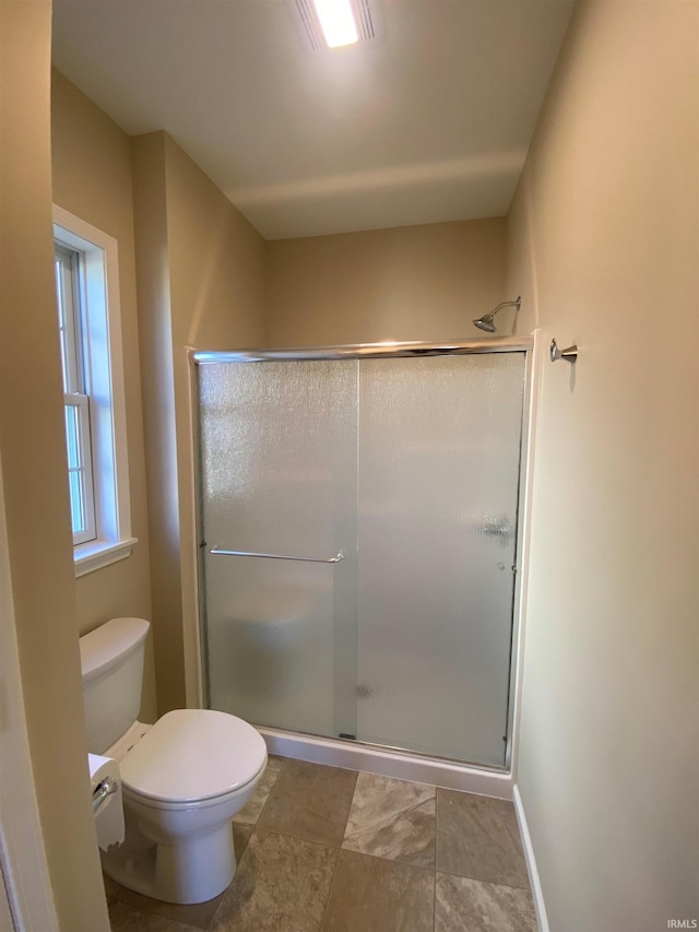 bathroom featuring toilet, a shower stall, and baseboards