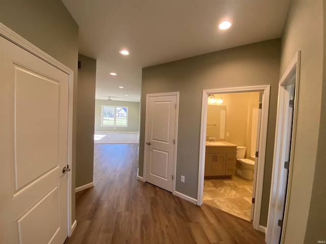 corridor with recessed lighting, dark wood-style flooring, baseboards, and a sink