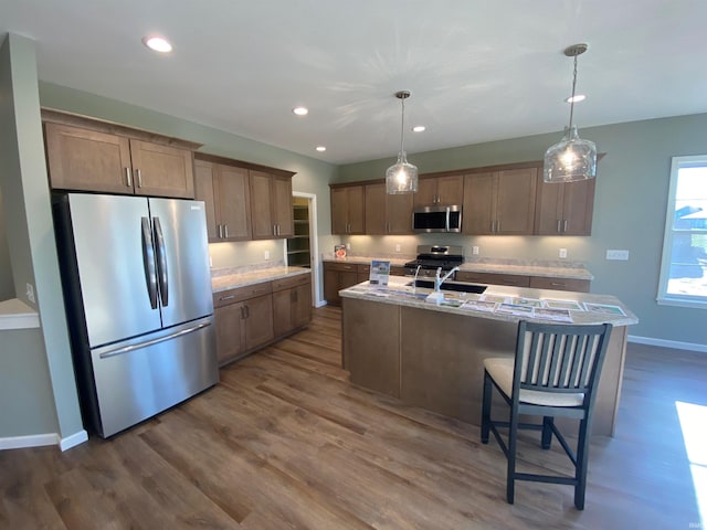 kitchen featuring baseboards, recessed lighting, dark wood-type flooring, a center island with sink, and stainless steel appliances