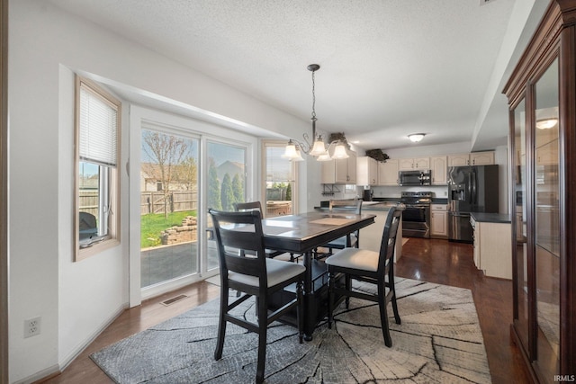 dining space featuring a notable chandelier, a textured ceiling, visible vents, and dark wood finished floors