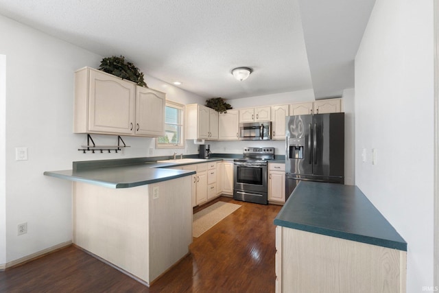 kitchen with a sink, appliances with stainless steel finishes, dark countertops, dark wood-type flooring, and a peninsula