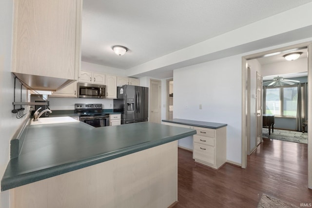 kitchen featuring dark wood-style floors, a sink, a peninsula, dark countertops, and appliances with stainless steel finishes