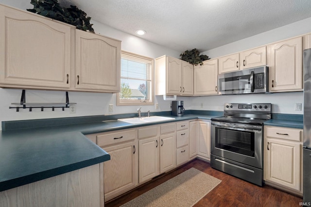 kitchen featuring stainless steel appliances, dark countertops, a sink, dark wood-style floors, and a textured ceiling