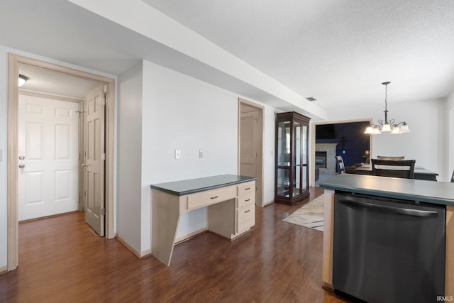 kitchen featuring stainless steel dishwasher, dark countertops, dark wood-style floors, a glass covered fireplace, and hanging light fixtures