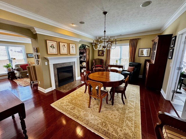 dining room with a textured ceiling, a tiled fireplace, baseboards, a chandelier, and hardwood / wood-style flooring