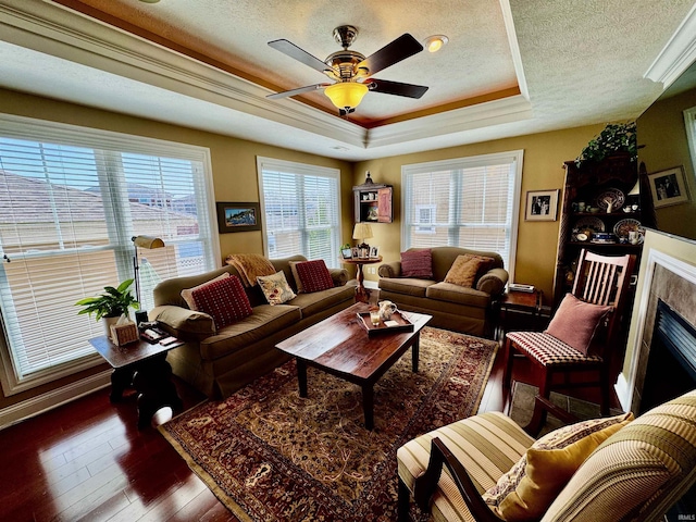 living area with a tray ceiling, a textured ceiling, dark wood-style floors, a ceiling fan, and a fireplace