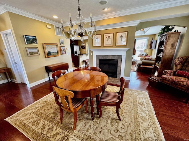 dining area with a fireplace, ornamental molding, arched walkways, baseboards, and a chandelier
