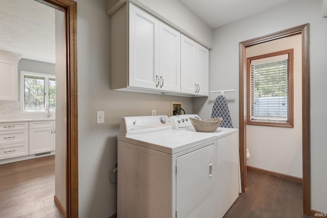 clothes washing area with cabinet space, wood finished floors, washing machine and clothes dryer, and baseboards