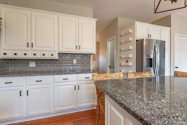 kitchen with decorative backsplash, dark stone counters, stainless steel fridge with ice dispenser, and white cabinets