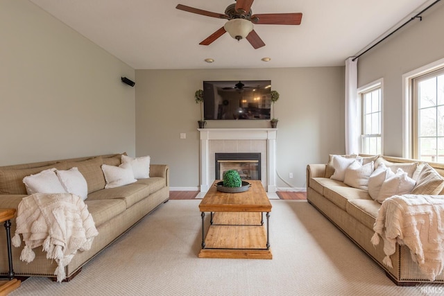 living room featuring wood finished floors, ceiling fan, a tiled fireplace, and baseboards