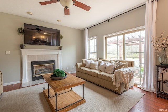 living area with a tiled fireplace, baseboards, wood finished floors, and ceiling fan