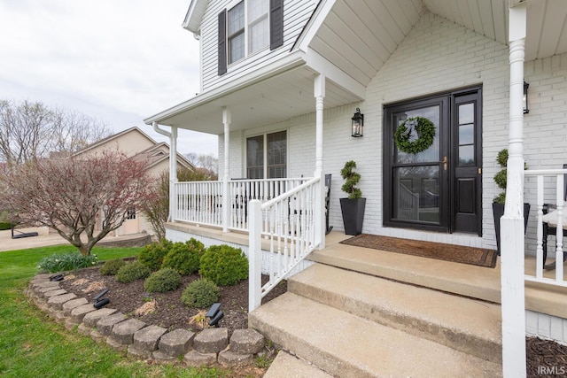view of exterior entry featuring covered porch and brick siding