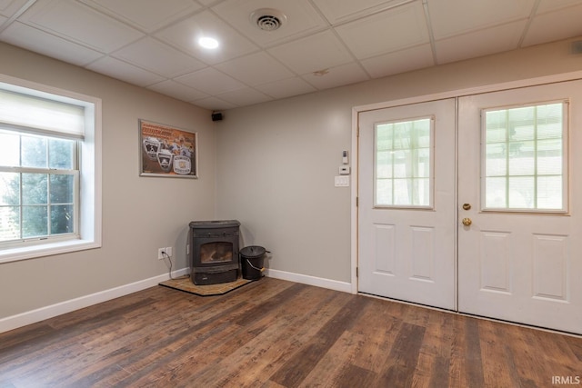 entrance foyer featuring baseboards, a wood stove, visible vents, dark wood finished floors, and a drop ceiling