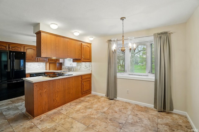 kitchen with light countertops, a chandelier, brown cabinets, black appliances, and backsplash