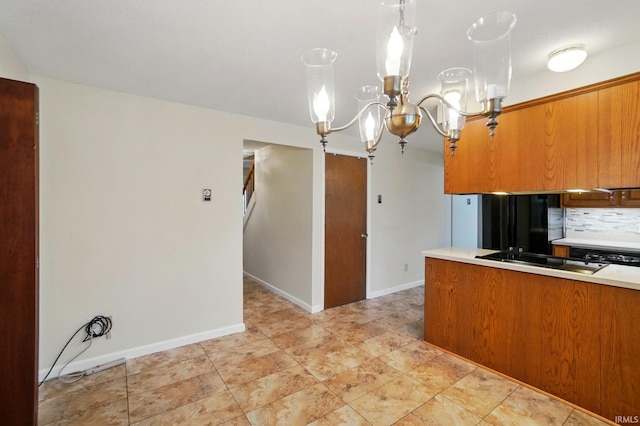 kitchen with brown cabinetry, a chandelier, light countertops, black electric stovetop, and decorative backsplash