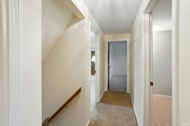 hallway featuring light carpet, an upstairs landing, and a textured ceiling
