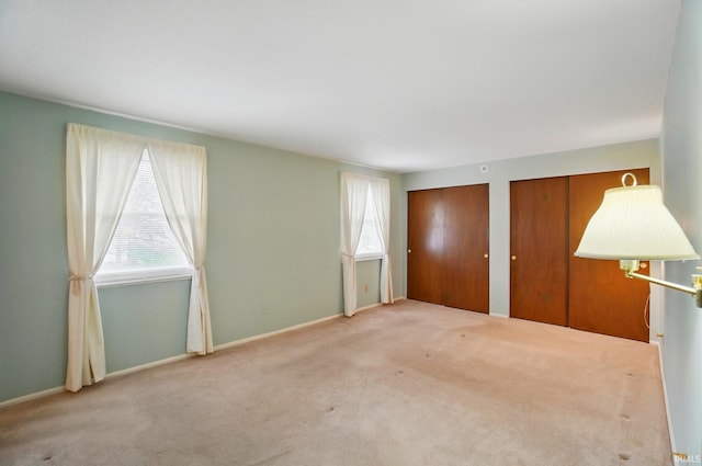 unfurnished bedroom featuring carpet flooring, baseboards, and multiple closets
