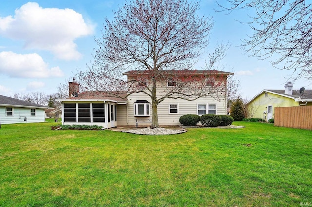 back of house with a sunroom, a chimney, fence, and a lawn